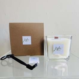 White candle in a clear glass container beside a brown box and black ribbon