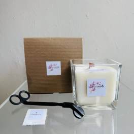 White candle in a square glass holder with a black wick trimmer and boxed packaging