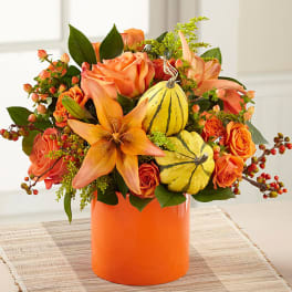 Orange floral arrangement with pumpkins in a bright vase
