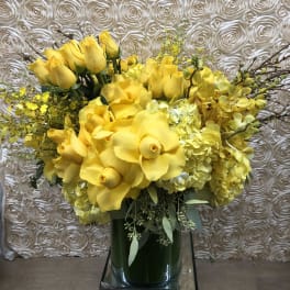 Yellow floral arrangement with roses and orchids in a glass vase