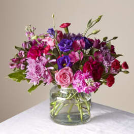 Mixed bouquet of pink roses, purple blooms, and red flowers in a clear glass vase
