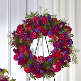 Heart-shaped floral wreath with pink roses and purple flowers on a stand