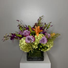 Lavender roses and orange lilies in a square glass vase