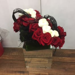 Red and white roses arranged in a square glass vase with black handles