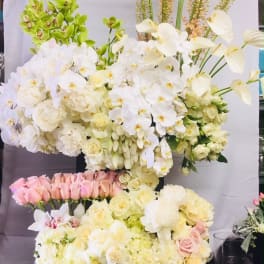 Large white floral arrangement with orchids and roses in a black container