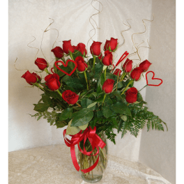 Red roses in a glass vase with red heart picks and ribbon