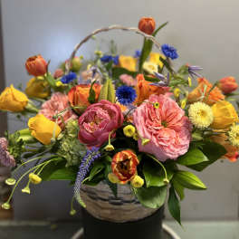 Basket arrangement of pink and yellow flowers with blue accents