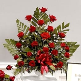 Tall arrangement of red roses in a white pedestal vase with a red bow