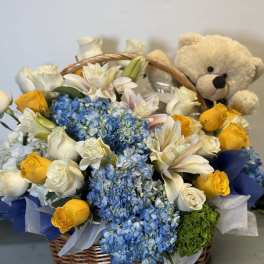 Basket of blue hydrangeas, white roses, yellow roses, and a teddy bear