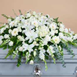 White floral casket spray with trailing greenery on a gray casket