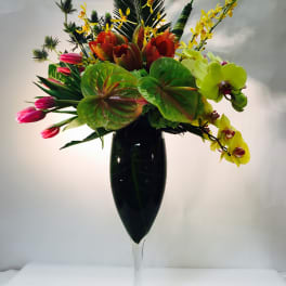 Tropical flower arrangement in a tall glass vase with orchids and tulips