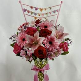 Pink and red flower bouquet in a glass vase with a Happy Valentine's Day topper