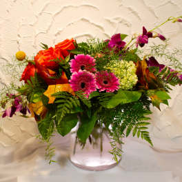 Mixed bouquet of orange roses, pink gerberas, and purple orchids in a glass vase