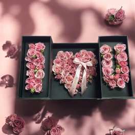 Pink roses arranged in three black gift boxes on a pink background