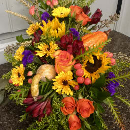 Autumn floral arrangement with sunflowers, orange roses, and a pumpkin accent