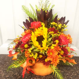 Autumn floral arrangement in a pumpkin-shaped container with sunflowers and daisies
