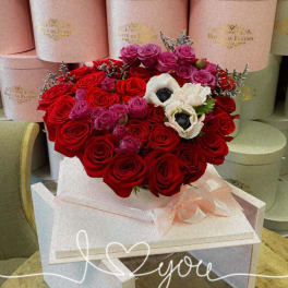 Heart-shaped bouquet of red and pink roses with white flowers in a pink box