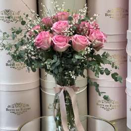 Pink roses in a clear glass vase with eucalyptus and a pink ribbon