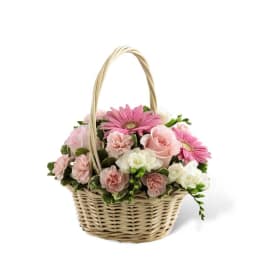 Small woven basket of pink gerbera daisies, roses, and carnations with white accent blooms