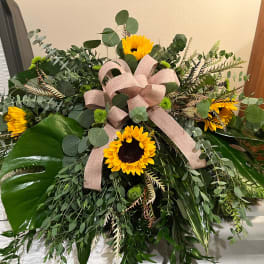 Large floral spray with sunflowers, greenery, and a pink ribbon bow