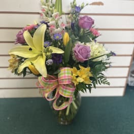 Mixed bouquet with yellow lilies, pink roses, and a plaid ribbon in a glass vase