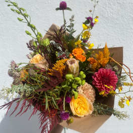 Hand-tied bouquet with orange, pink, and yellow flowers in brown paper