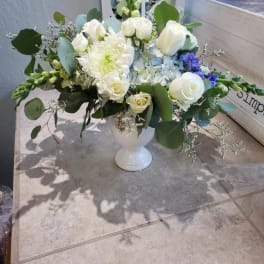 White floral arrangement in a white pedestal vase with blue accents