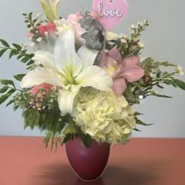 Bouquet of white lilies and pink flowers in a purple vase with a pink heart pick