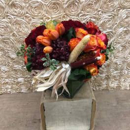 Bouquet of orange and burgundy flowers with decorative corn in a square box
