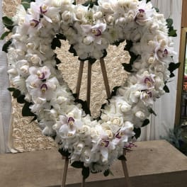 Heart-shaped white floral wreath on an easel with orchids and roses