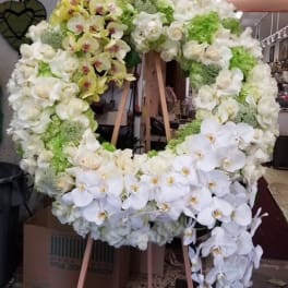 Large white floral wreath on a wooden stand with cascading orchids
