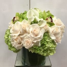 White roses and calla lilies arranged with green hydrangeas in a glass vase