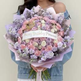 Large pastel bouquet of roses, carnations, and lilac flowers with a birthday ribbon