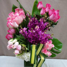 Pink roses and purple orchids arranged in a glass vase
