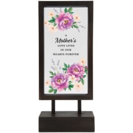 Framed floral memorial sign on a dark stand with the words "A Mother's Love Lives in Our Hearts Forever"