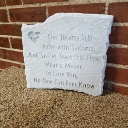 White memorial plaque with an engraved sympathy poem leaning against a brick wall