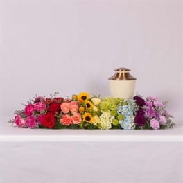 Long floral casket spray with multicolored flowers and a gold urn