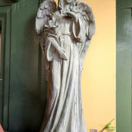 A carved angel statue holding flowers stands against a yellow wall.