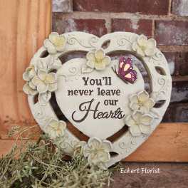 Heart-shaped decorative plaque with flowers and a butterfly, reading "You'll never leave our Hearts"