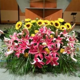 Large stage arrangement of pink lilies, yellow sunflowers, and yellow blooms in a low, wide design