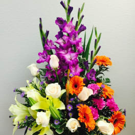 Tall mixed arrangement with purple flowers, orange gerberas, white roses, and yellow lilies in a basket