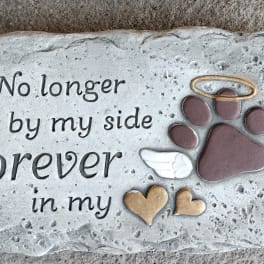 Memorial stone with paw print, halo, wings, and the words "No longer by my side Forever in my"