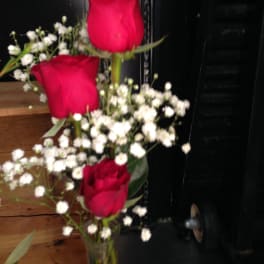 Three red roses with white baby's breath in a clear glass vase