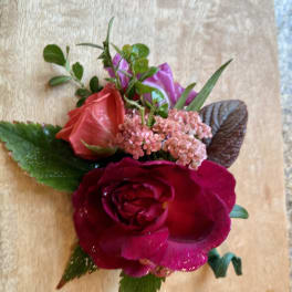 Small floral corsage with red and pink roses on a wooden surface