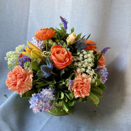 Mixed bouquet of orange roses, carnations, and purple flowers in a green vase