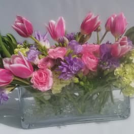Low pink tulip, hydrangea, ranunculus, and purple freesia arrangement in a rectangular glass vase