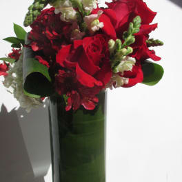 Tall glass cylinder of red roses and white snapdragons with green leaves lining the vase