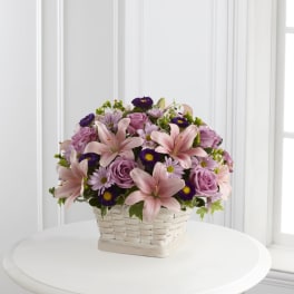 Pink lilies, roses, and purple daisies in a white basket
