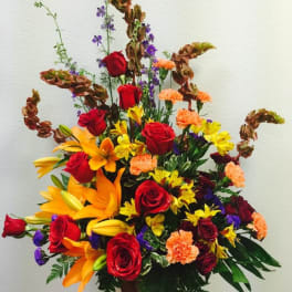 Tall mixed arrangement of red roses, orange lilies, and assorted blooms in a wooden container