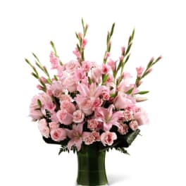 Tall pink bouquet of lilies, roses, and carnations in a green-wrapped glass vase